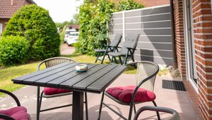 Una terrazza esterna con tavolo e sedie, un muro in mattoni e un siepe.