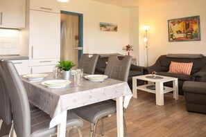 A modern living room with a dining area, grey furniture, a small table, and a painting on the wall. - Cozy vacation apartment in a quiet location in Hooksiel - ideal for families and couples looking for relaxation by the North Sea. (Hooksiel)