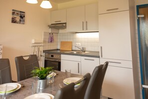 A modern kitchen with white cabinets, a stainless steel sink, and a dining area with a table set for two. - Cozy vacation apartment in a quiet location in Hooksiel - ideal for families and couples looking for relaxation by the North Sea. (Hooksiel)