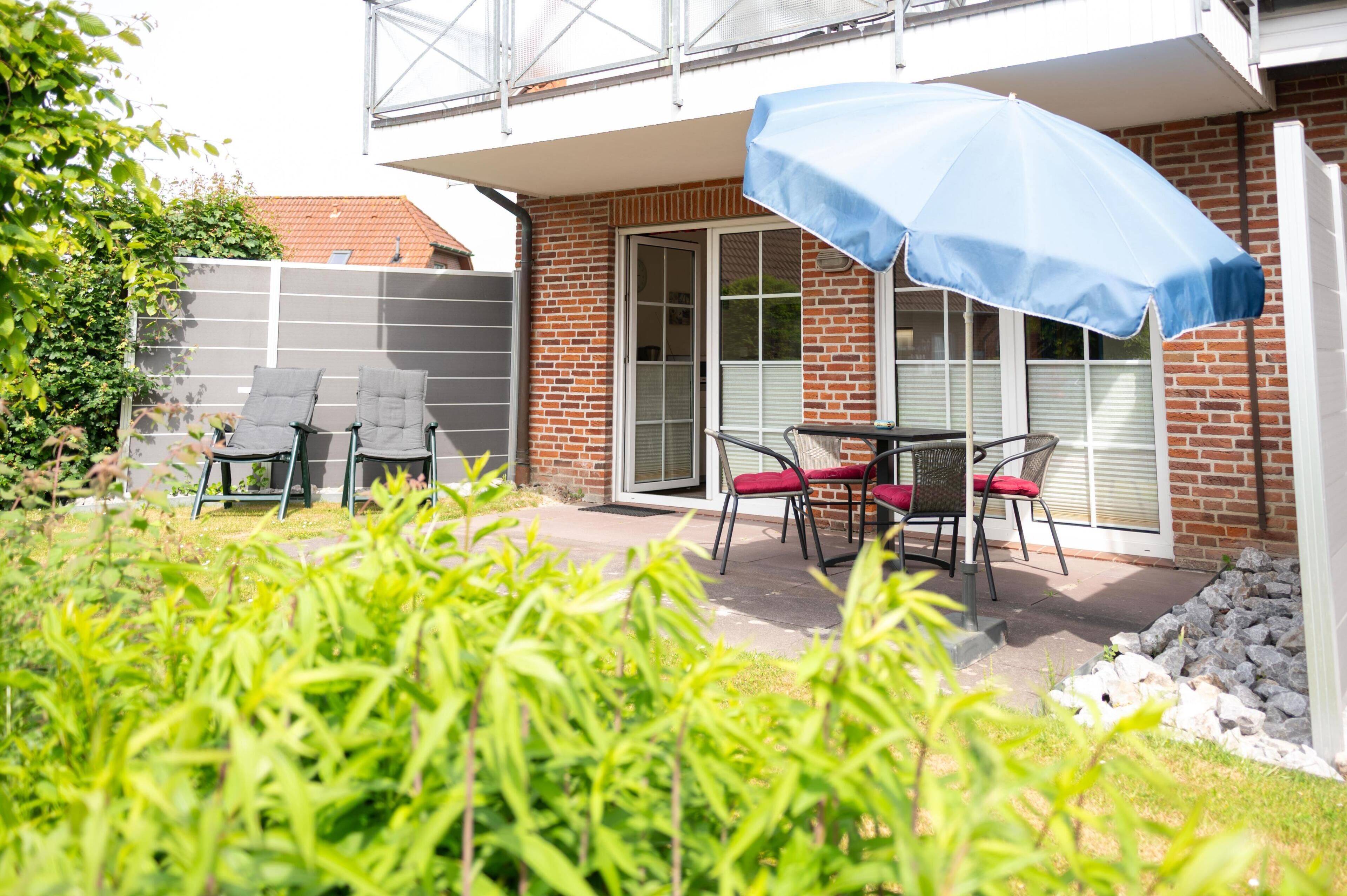 Une terrasse avec des meubles d’extérieur, un parasol bleu et un bâtiment en briques doté d’une porte en verre.