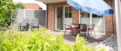 Un patio con mobiliario exterior, una sombrilla azul y un edificio de ladrillo con puerta de cristal.