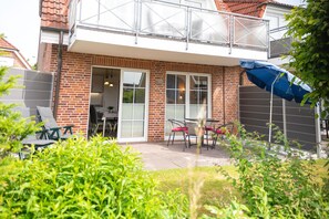 A brick house with a balcony, a dining area with chairs and a table, and a blue umbrella. - Cozy vacation apartment in a quiet location in Hooksiel - ideal for families and couples looking for relaxation by the North Sea. (Hooksiel)