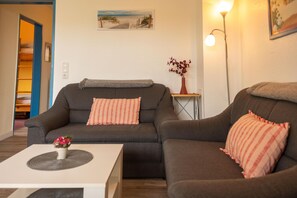 Een woonkamer met een bank, een kleintje tafeltje met een vaas, een lamp en een schilderij aan de muur.