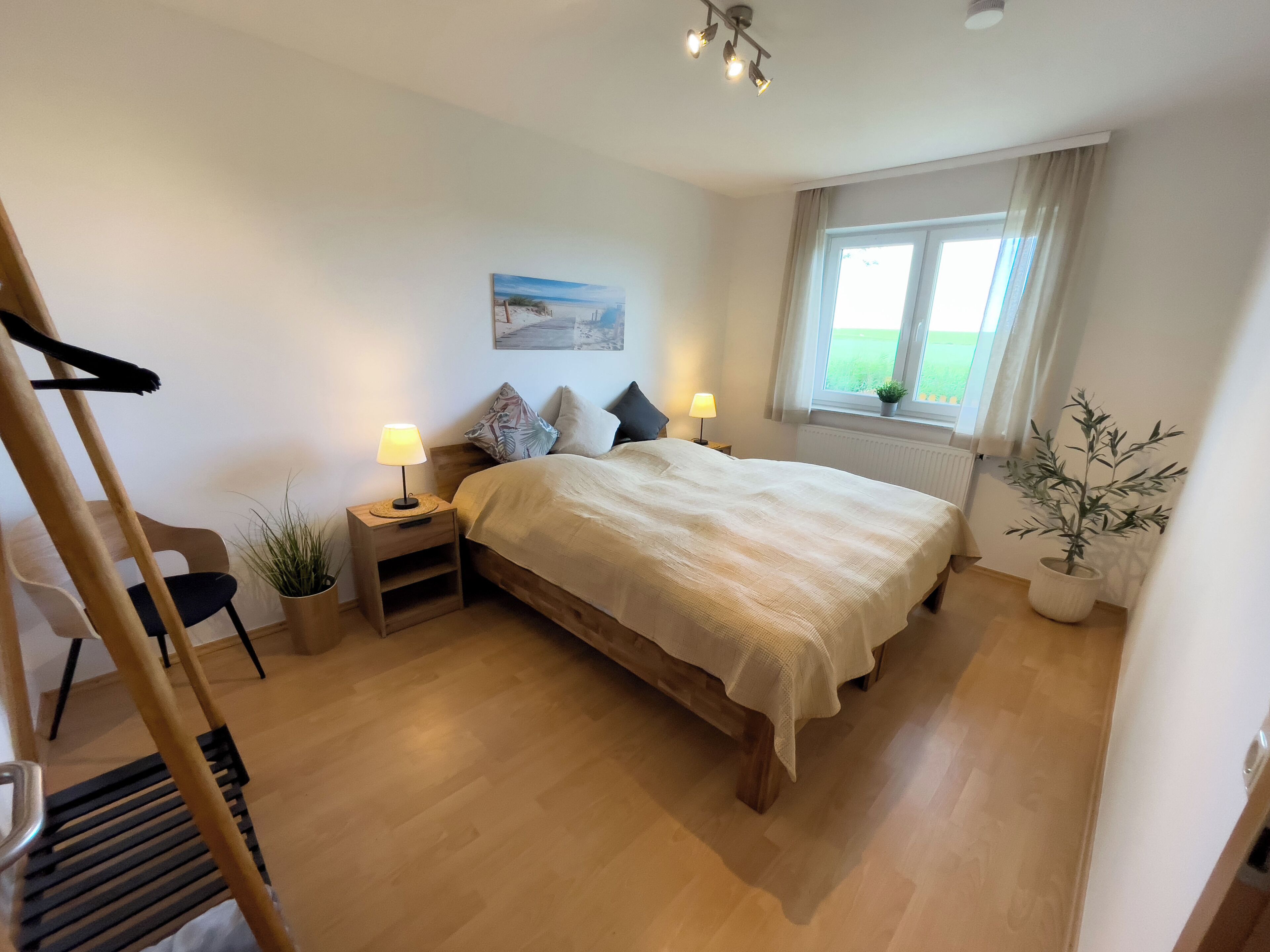 A bedroom with a bed, bedside tables, a window with curtains, a plant, and a painting on the wall.