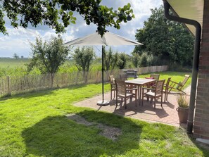 Eine Terrasse mit Tisch und Stühlen, einem Grill und Blick auf ein grünes Feld.