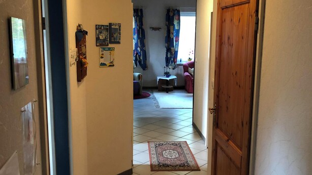 Käytävän lattia on laatoitettu, siinä on puinen ovi ja pieni pöytä, jonka päällä on matto.