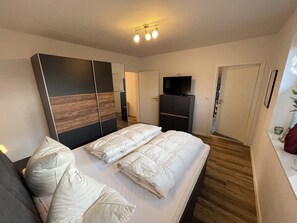 A bedroom with a bed, a wardrobe, a television, and a door. - Modern bungalow directly on the Wangermeer with fenced garden, wooden sauna, two bathrooms, fully equipped kitchen - ideal for families, couples and vacations with dogs. (Wangerland)