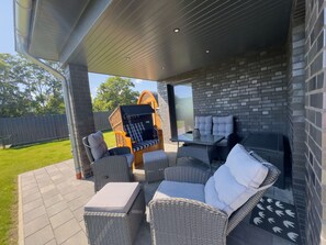 An outdoor patio with wicker furniture, a glass table, and a brick wall. - Modern bungalow directly on the Wangermeer with fenced garden, wooden sauna, two bathrooms, fully equipped kitchen - ideal for families, couples and vacations with dogs. (Wangerland)