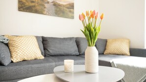 En stue med en grå sofa, en hvid vase med tulipaner, et stearinlys og et rundt bord.