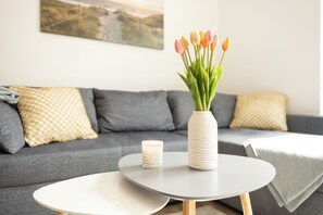 A living room with a grey sofa, a white vase with tulips, a candle, and a round table. - Modern vacation home with garden on the Wangermeer - Mee(h)rzeit offers comfort, style and relaxation for the whole family, including four-legged friends. (Wangerland)