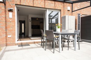 An open sliding door leading to a kitchen, a dining table with chairs, and a white cabinet. - Modern vacation home with garden on the Wangermeer - Mee(h)rzeit offers comfort, style and relaxation for the whole family, including four-legged friends. (Wangerland)