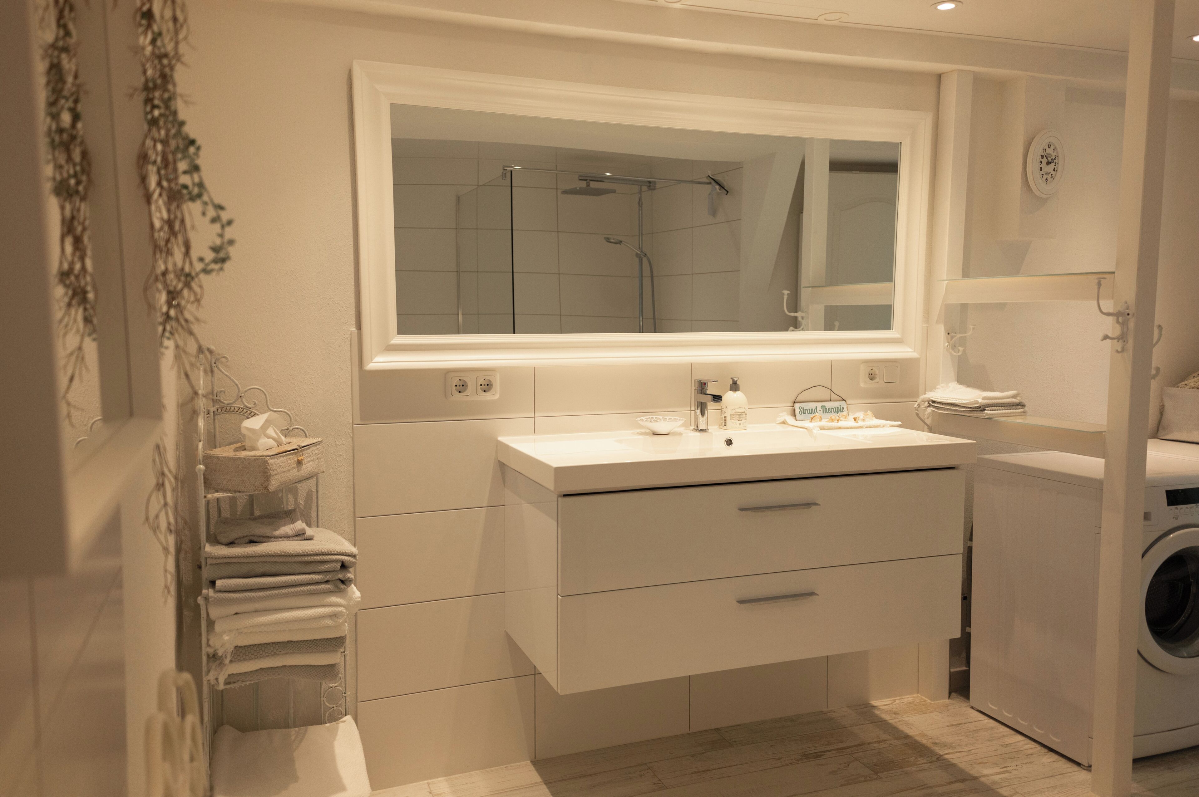 Un baño moderno con un espejo grande, un lavamanos integrado, una ducha y una lavadora.