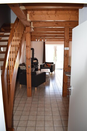 A wooden staircase leading to a living area with a fireplace, sofa, and tiled floor. - The Nordlys vacation home on the North Sea offers modern comfort with a wood-burning stove, south-west-facing terrace and fenced garden - perfect for families and couples. (Hooksiel)