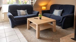 Una sala de estar acogedora con dos sofás azul oscuro, una mesa de centro de madera y una lámpara.