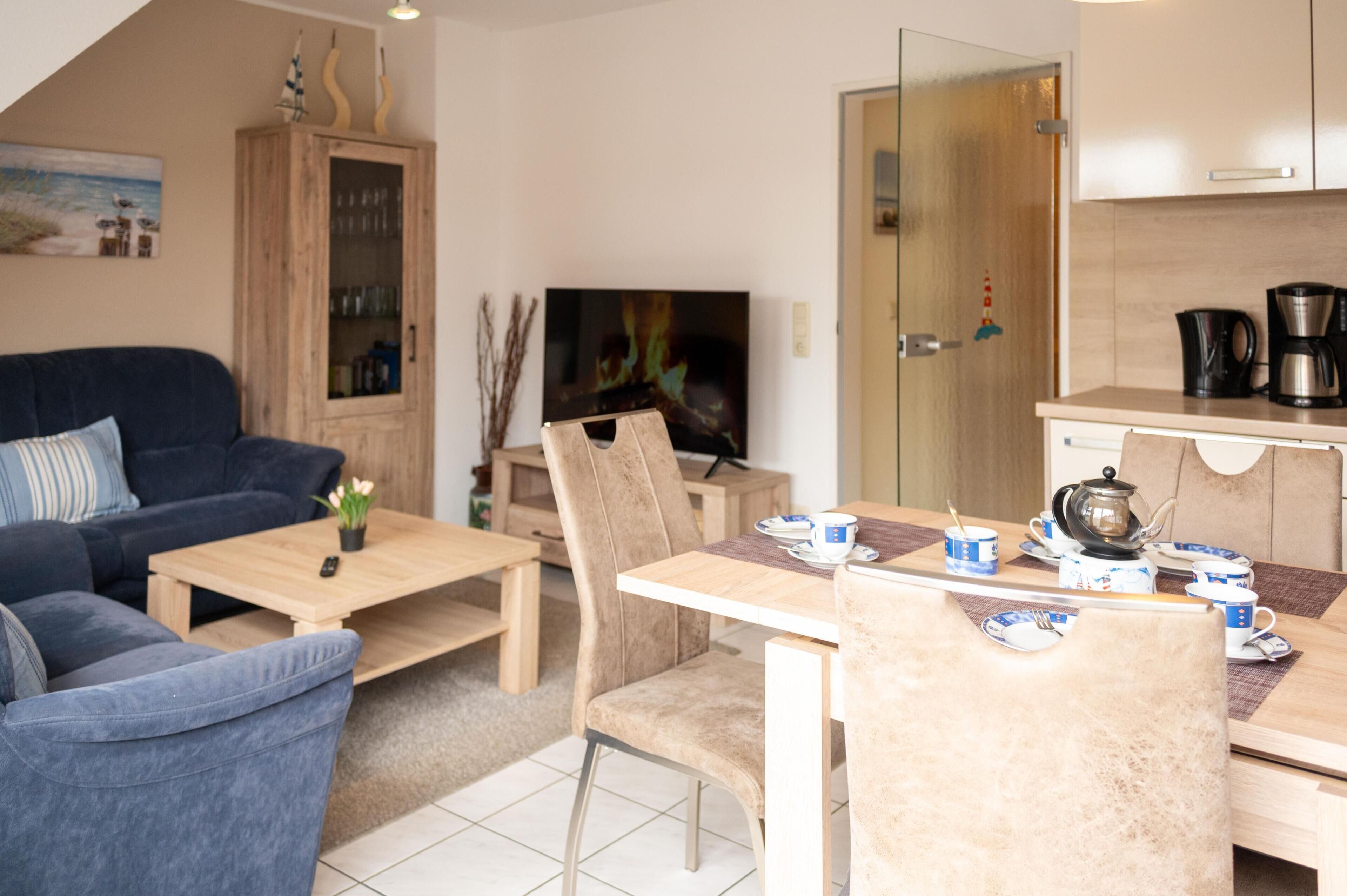 A living room with a sofa, coffee table, TV, and a dining area with chairs and a table set for tea.
