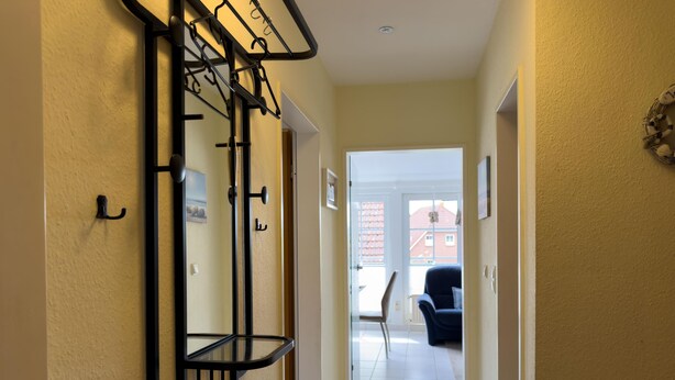 Un pasillo con un perchero, una puerta con pomo y vistas a un espacio exterior con una silla y un edificio.