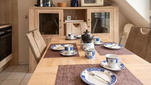 Comedor con mesa de madera dispuesta para dos personas, con platos y tazas azules y blancos, además de una tetera.