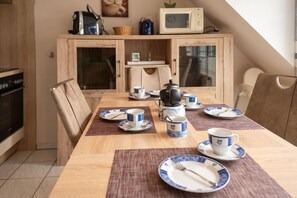 Ein Essbereich mit einem Holztisch, gedeckt für zwei Personen, mit blauen und weißen Tellern, Tassen und einem Wasserkocher.