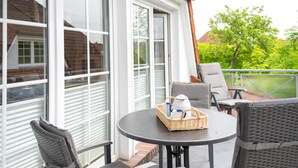 Un patio cubierto con una mesa redonda, dos sillas y una cesta de mimbre con una tetera y tazas.