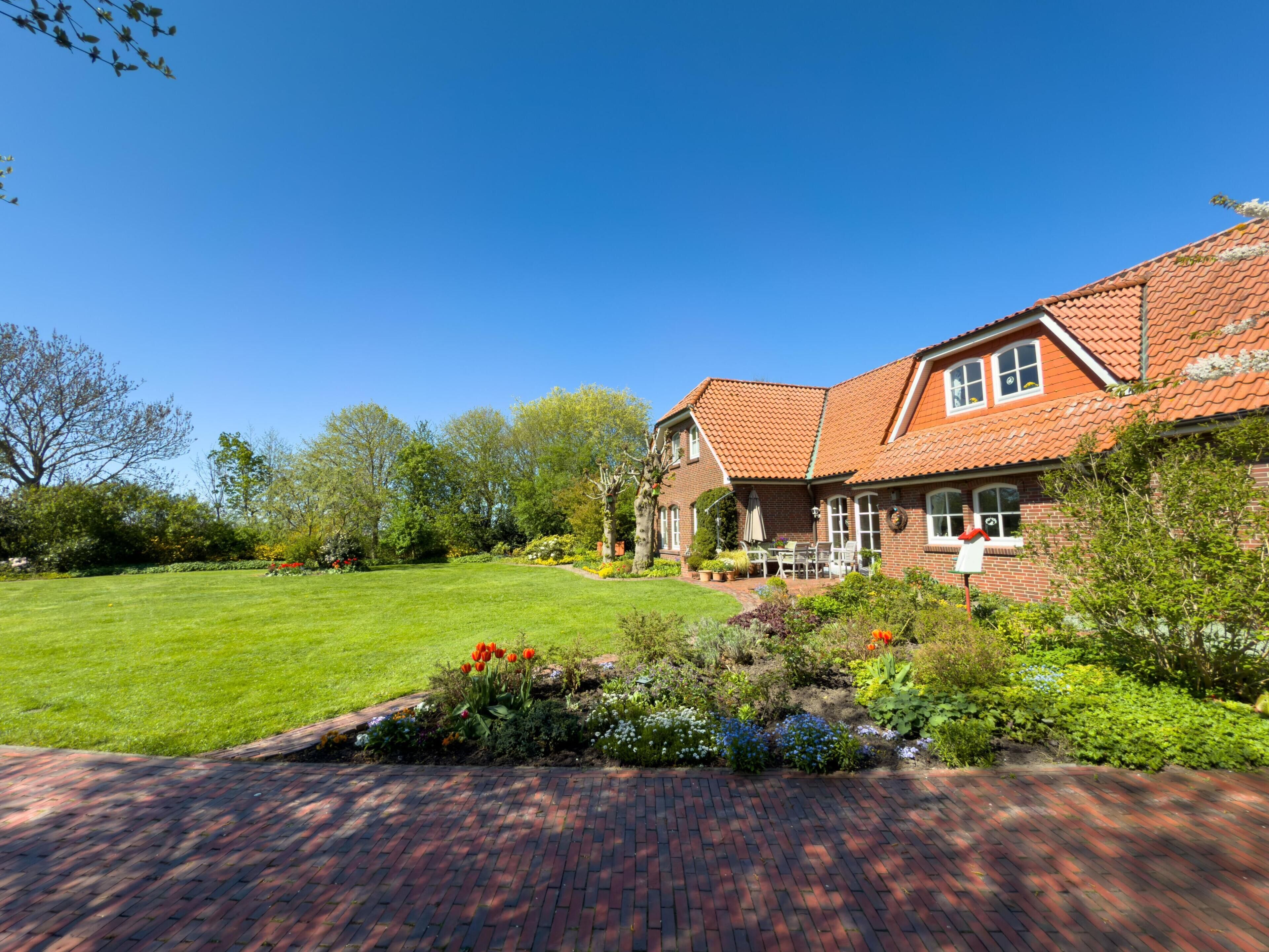 A two-story house with a red-tiled roof, a brick exterior, and a well-maintained garden with various plants and flowers.