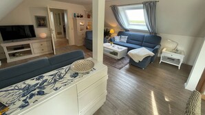 Una sala moderna con un sofá, televisor y una zona de comedor con mesa y sillas.