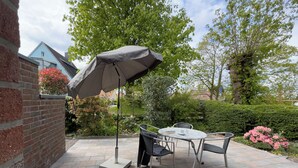 Een terras buiten met een tafel, stoelen, een parasol en een bakstenen muur.