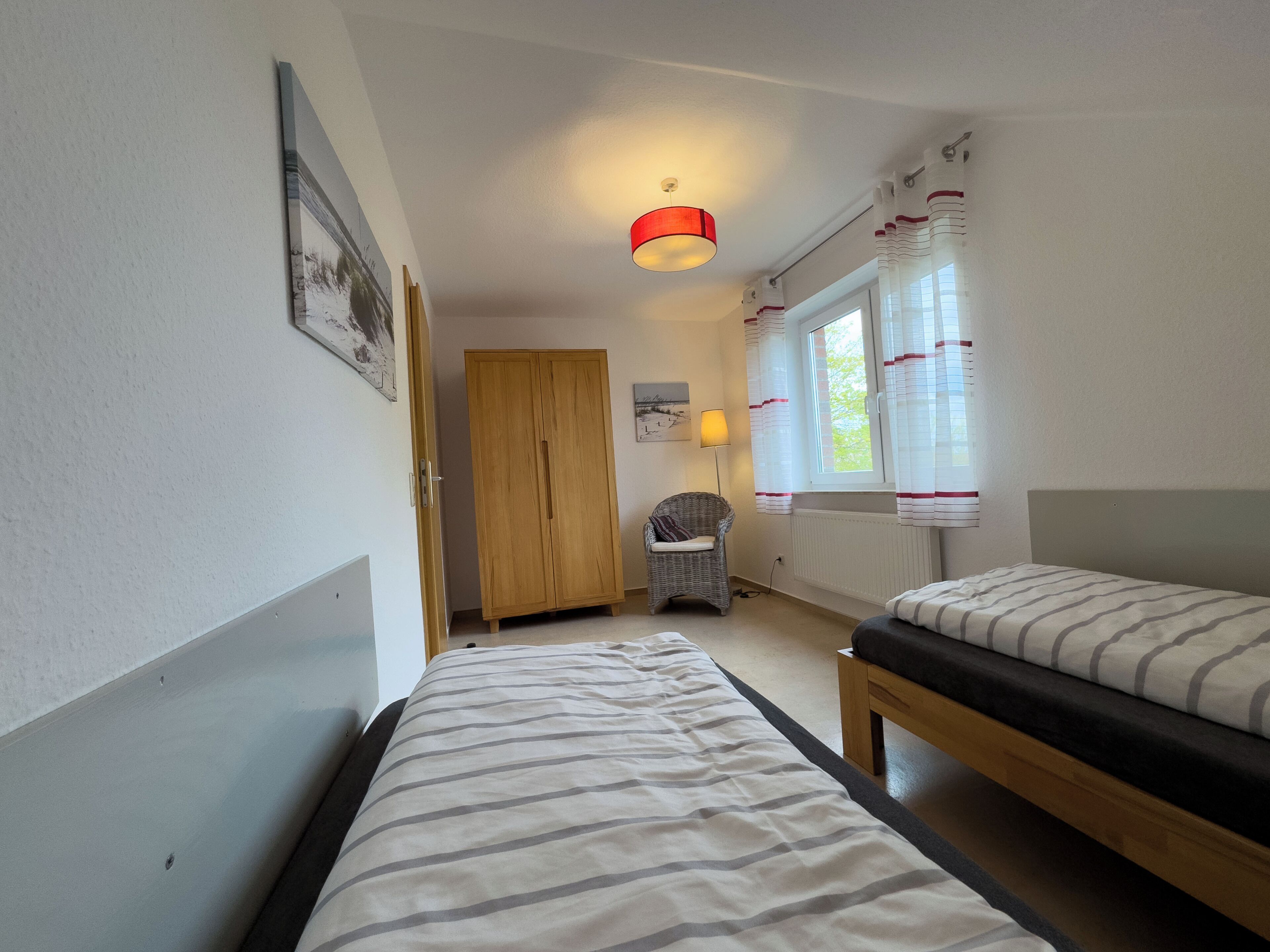 Une chambre avec deux lits, une armoire, une chaise, une lampe et une fenêtre avec des rideaux.