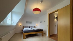 Een slaapkamer met een schuine kap, een bed, een nachtkastje, een wandlamp, een deur en een raam.