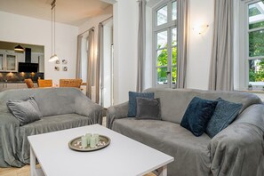 A modern living room with grey sofas, a white coffee table, and a kitchen in the background.