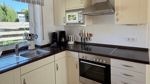 Een keuken met een fornuis, oven, magnetron en een raam met uitzicht op groen.