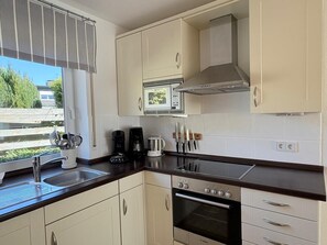 A kitchen with a stove, oven, microwave, and a window with a view of greenery.