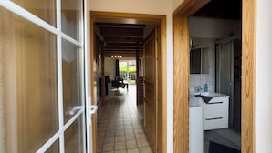 A corridor leading to a living area with a sofa and chairs, a wooden ceiling, and a bathroom with a sink and mirror. - The Tegeler Plate 26 vacation home offers stylish living comfort, bright rooms and a sunny garden for a relaxing family vacation. (Hooksiel)