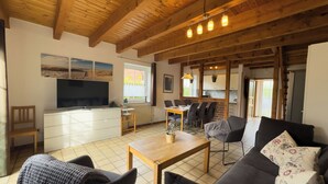 A living room with a sofa, a coffee table, a TV, and a dining area with chairs and a table. - The Tegeler Plate 26 vacation home offers stylish living comfort, bright rooms and a sunny garden for a relaxing family vacation. (Hooksiel)