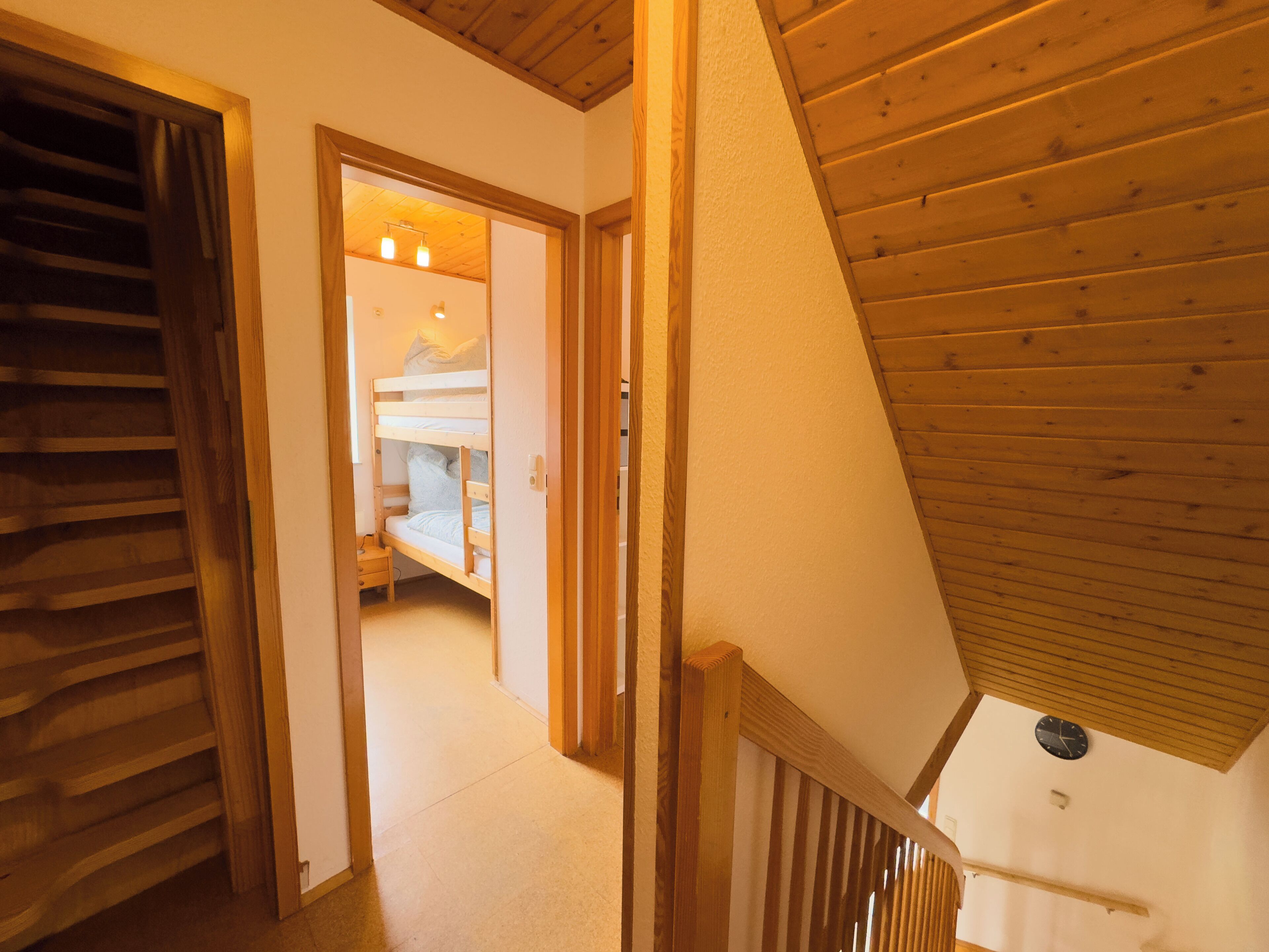 Een houten trap leidt naar een slaapkamer met een stapelbed en een klein nachtkastje.
