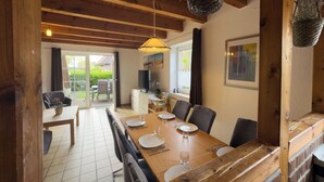 A dining area with a wooden table set for four, a television, and a view of the outdoors. - The Tegeler Plate 26 vacation home offers stylish living comfort, bright rooms and a sunny garden for a relaxing family vacation. (Hooksiel)