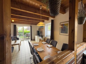 A dining area with a wooden table set for four, a television, and a view of the outdoors. - The Tegeler Plate 26 vacation home offers stylish living comfort, bright rooms and a sunny garden for a relaxing family vacation. (Hooksiel)