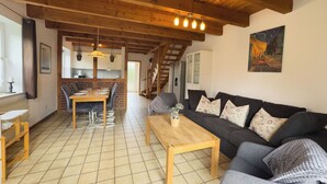 A spacious living area with a wooden ceiling, a dining table, a sofa, and a staircase leading to an upper floor. - The Tegeler Plate 26 vacation home offers stylish living comfort, bright rooms and a sunny garden for a relaxing family vacation. (Hooksiel)