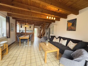 A spacious living area with a wooden ceiling, a dining table, a sofa, and a staircase leading to an upper floor. - The Tegeler Plate 26 vacation home offers stylish living comfort, bright rooms and a sunny garden for a relaxing family vacation. (Hooksiel)