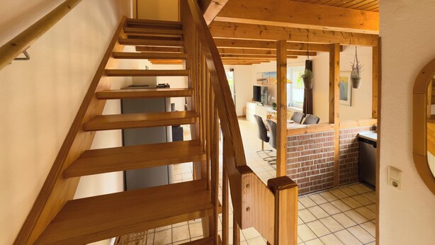 A wooden staircase leading to a living area with a brick wall, a dining table, and a hanging plant. - The Tegeler Plate 26 vacation home offers stylish living comfort, bright rooms and a sunny garden for a relaxing family vacation. (Hooksiel)