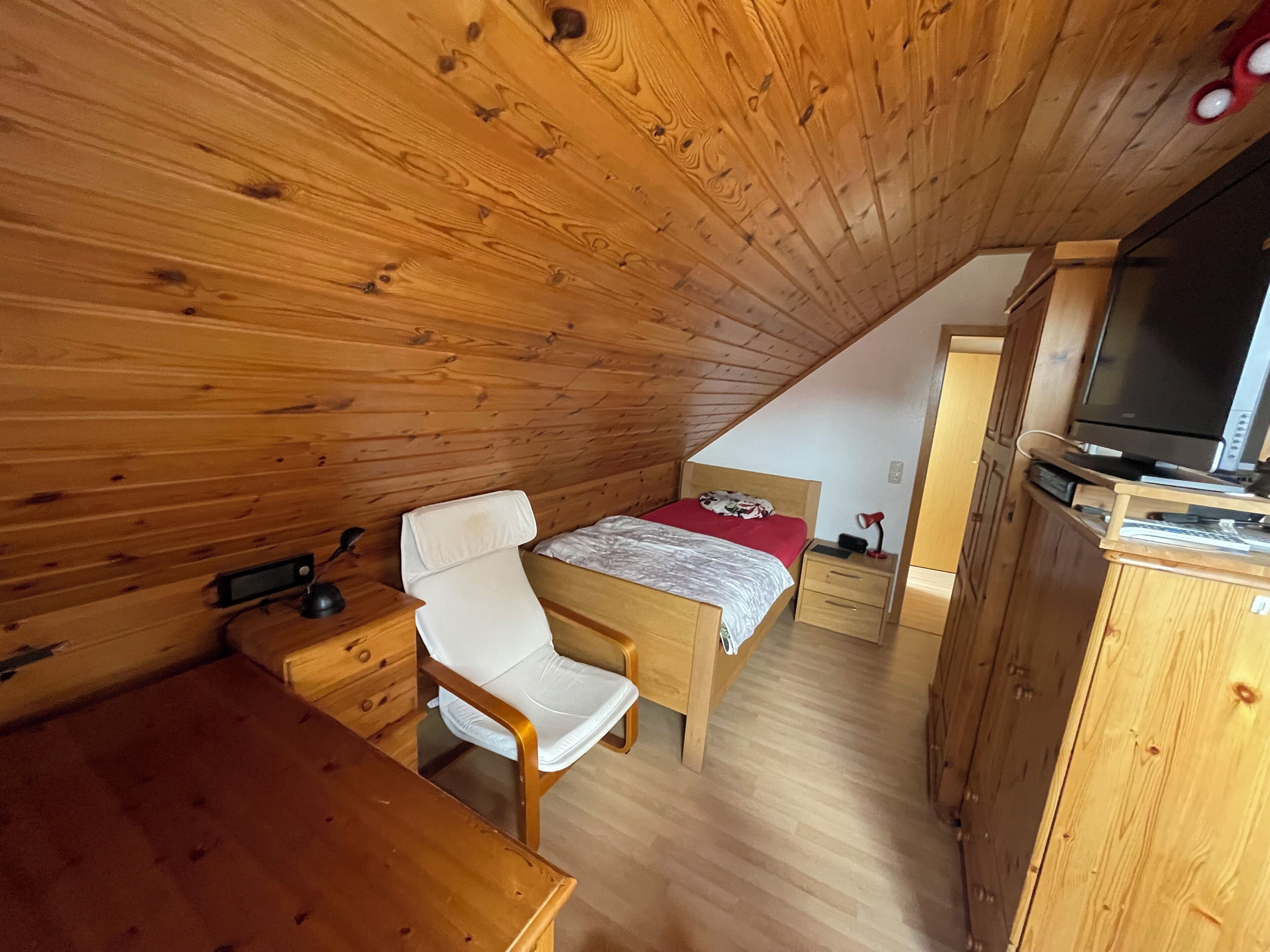 Une pièce en bois comprenant un lit, un bureau, une chaise, un téléviseur et une armoire.