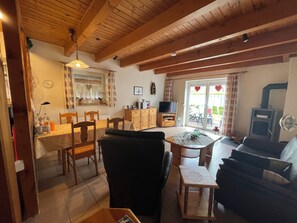 A cozy living area with a dining table, chairs, a sofa, a television, and a fireplace. - The charming Tillmann vacation home offers modern furnishings, a cozy wooden ambience and a sunny southwest-facing terrace - just a few minutes' walk from the dyke. (Hooksiel)