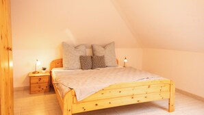 A bedroom with a wooden bed, two bedside tables, and a sloped ceiling. - The spacious Tillmann vacation home offers a cozy wooden ambience, modern comfort and an inviting garden - just a few minutes' walk from the dyke. (Hooksiel)