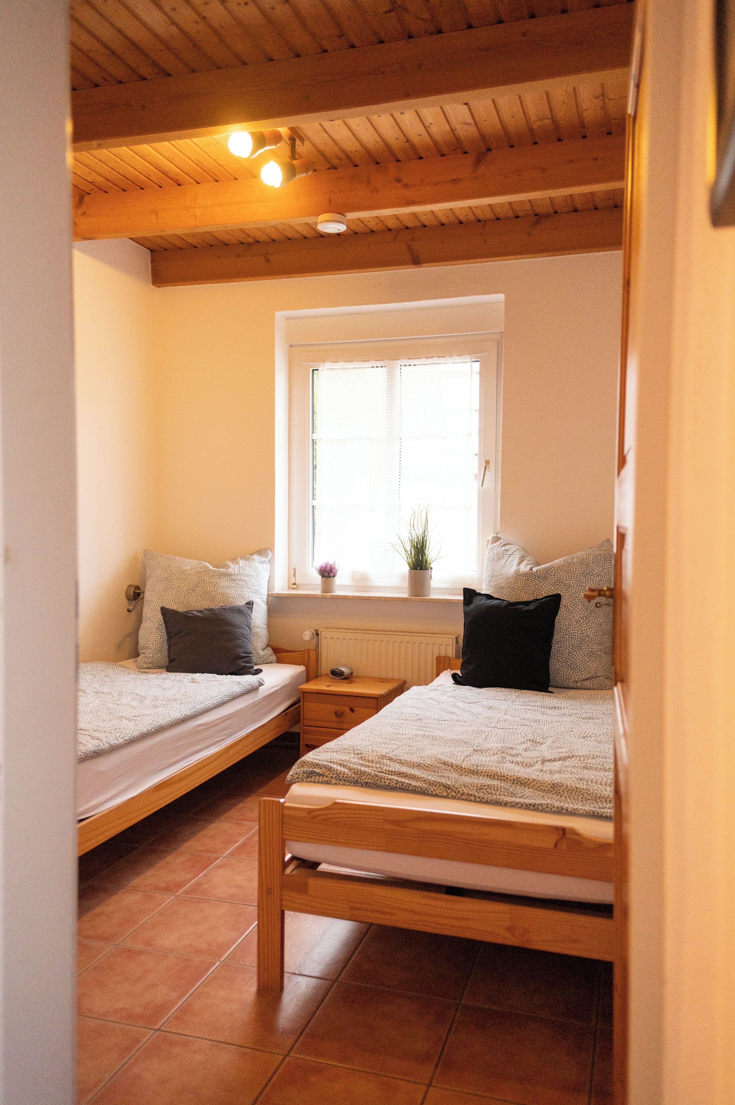 Quarto pequeno e aconchegante com duas camas de solteiro, janela com vista e teto de madeira.