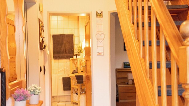 A hallway with a wooden staircase, a radiator, a potted plant, and a tiled floor. - The spacious Tillmann vacation home offers a cozy wooden ambience, modern comfort and an inviting garden - just a few minutes' walk from the dyke. (Hooksiel)