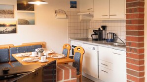 A kitchen with white cabinets, a brick archway, a dining table with chairs, and a hanging light fixture. - The spacious Tillmann vacation home offers a cozy wooden ambience, modern comfort and an inviting garden - just a few minutes' walk from the dyke. (Hooksiel)