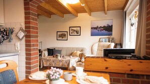 A cozy room with a dining table set for two, a sofa, and a television. - The spacious Tillmann vacation home offers a cozy wooden ambience, modern comfort and an inviting garden - just a few minutes' walk from the dyke. (Hooksiel)