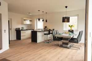 A modern kitchen with a dining area, featuring a central island, bar stools, pendant lighting, and a window with a view. - The modern vacation home Wanger Meerblick offers high-quality living comfort, three bedrooms, a fenced garden and a wonderful view of the Wangermeer - perfect for families and dog owners. (Wangerland)