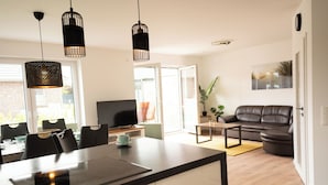 A modern kitchen with a dining area, a sofa, and a TV. - The modern vacation home Wanger Meerblick offers high-quality living comfort, three bedrooms, a fenced garden and a wonderful view of the Wangermeer - perfect for families and dog owners. (Wangerland)