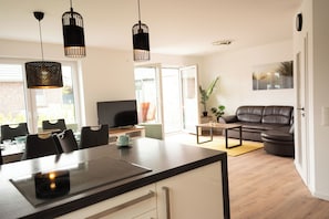 A modern kitchen with a dining area, a sofa, and a TV. - The modern vacation home Wanger Meerblick offers high-quality living comfort, three bedrooms, a fenced garden and a wonderful view of the Wangermeer - perfect for families and dog owners. (Wangerland)