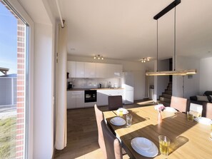 A modern kitchen with white cabinets, a dining area with a wooden table, and a staircase leading to another level. - The Wangermeer Perle I is a modern, spacious semi-detached house on the Wangermeer - ideal for families and groups looking for comfort and proximity to nature. (Wangerland)